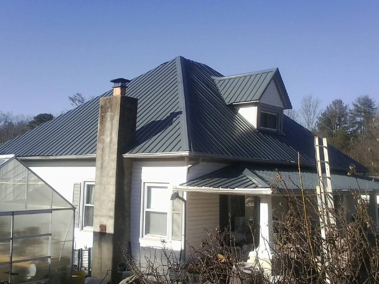 Dark blue standing seam metal roof on a white farmhouse with dormer — Slate & Tile Roof Repair by Roofing Brothers in Winslow