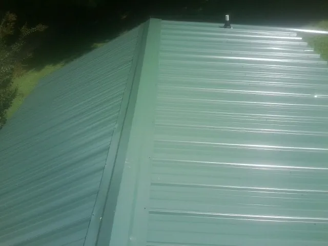 New green metal panels meeting at the ridge of a roof — Flat Roof Repair work by our crew in Winslow
