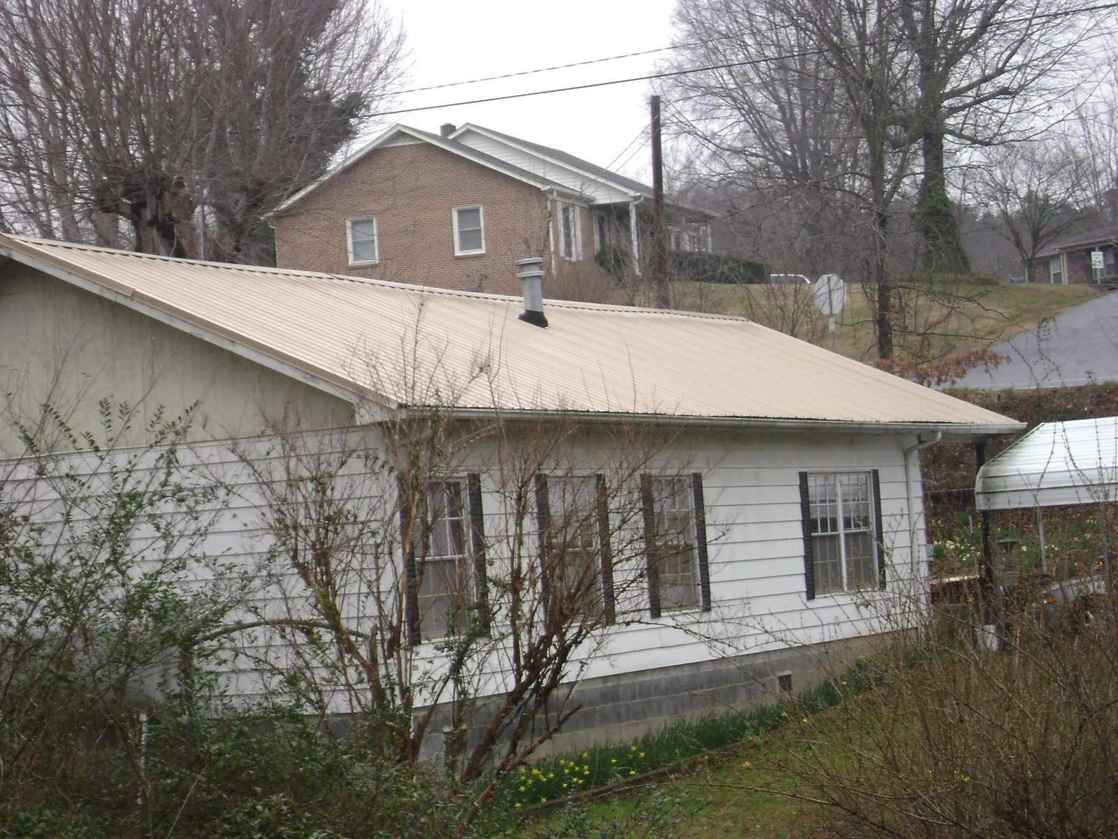 Tan metal roof on a white sided house set into a hillside — Commercial Roofing by Roofing Brothers in Winslow